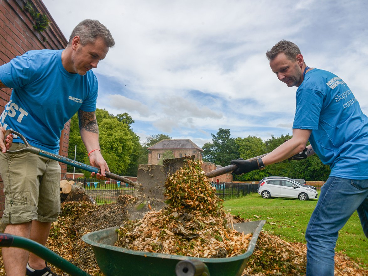 Two men shovelling leaves into a wheelbarrow