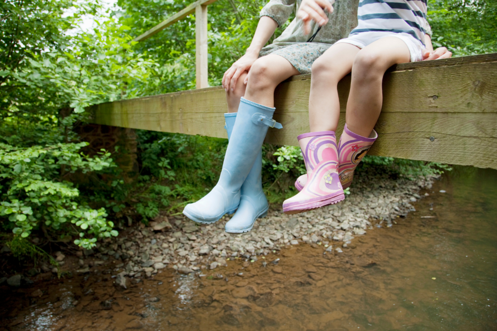 Two children sitting on bridge wearing wellies