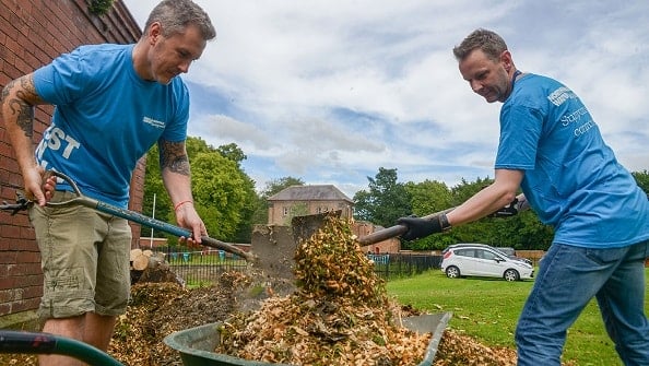 Two Northumbrian Water employees digging dirt and leaves into a wheelbarrow