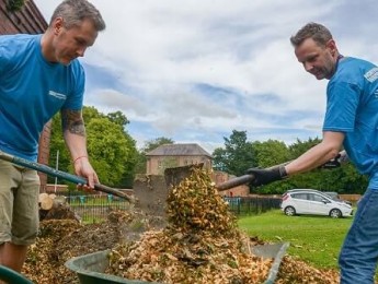 Two Northumbrian Water employees in the community shoveling leaves into a wheelbarrow